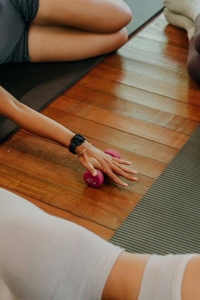 A hand resting on a small weight beside a mat on a wooden floor